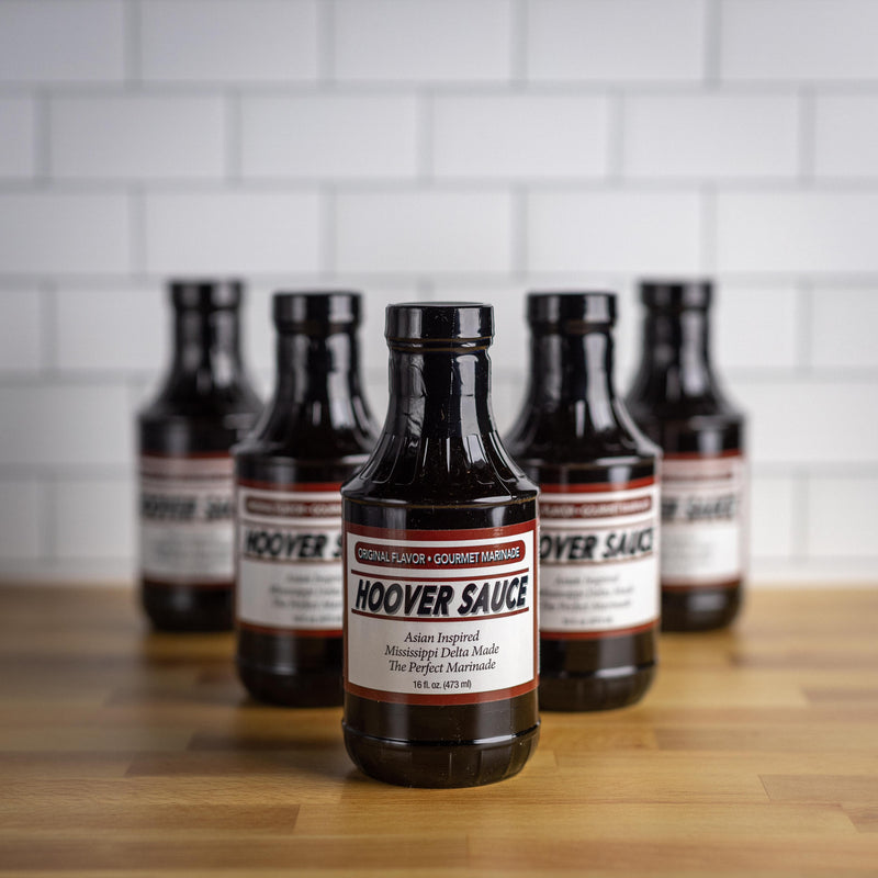 Multiple bottles of Hoover Sauce arranged on a wooden surface with white tile background.